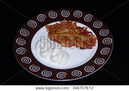 Potato Pancakes With Sour Cream On A Round Plate On A Black Background