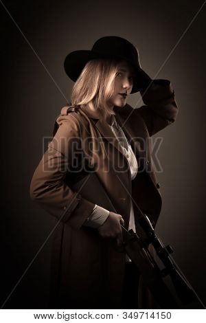 Mafioso Woman In A Brown Cloak And Black Hat With Airguns In Her Hands. Gangster Style Photo Shoot.