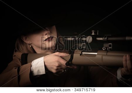 A Woman In A Brown Cloak And A Black Hat With Airguns In Her Hands Looks Into The Sight. Blurred Foc