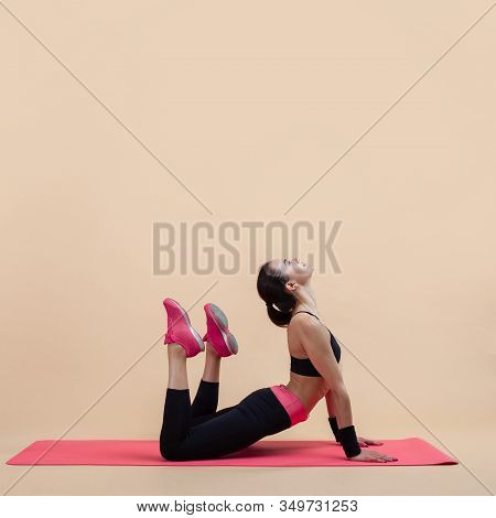 A Young Attractive Girl With A Ponytail, A Brunette, Is Lies In A Cobra Pose With Knees Bent, Doing 