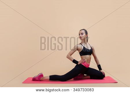 Young Attractive Girl With A Ponytail, Brunette, Sitting In The Pose Of A Pigeon With His Hands On A