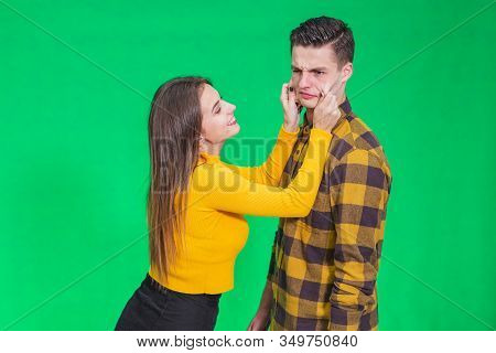 Girl Pinching Guys Cheeks, Making Fyn, He Is Scowling His Face, Looking Completely Annoyed.