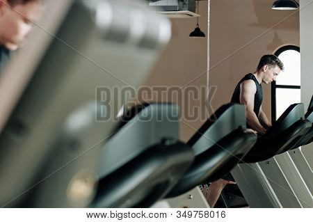 Serious Fit Young Man Running On Threadmill In Gym In The Morning