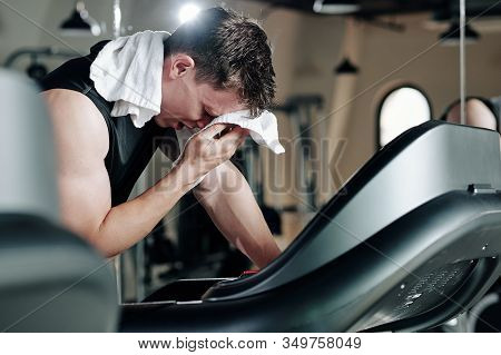 Sportsman Wiping Sweat From His Forehead After Running On Threadmill In Gym