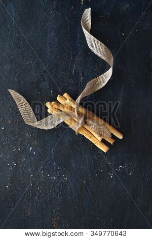Bunch Of Grissini Breadsticks Tied Together With A Ribbon On Dark Background, Breadsticks Center Lay