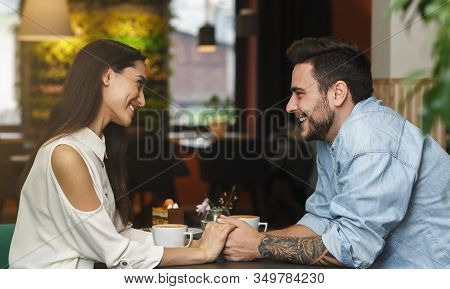 Lovely Couple In Love Flirting And Talking Holding Hands Having Date Sitting In Cozy Cafe. Romantic 