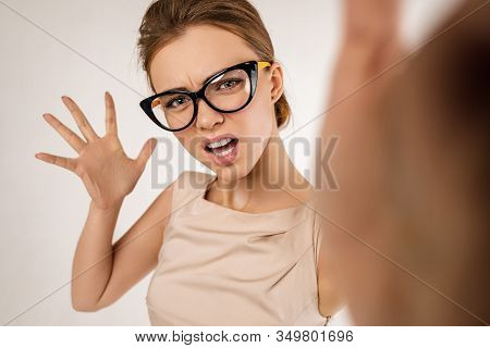 Portrait Of Angry Woman Wearing Glasses Gives A Slap In The Face. Girl Hits The Camera