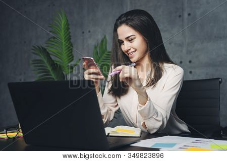 Woman Sitting At Workplace And Communicating In Social Network Using Smartphone. Young Executive Sen