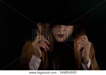 Retro Gangster Woman In A Brown Cloak And Black Hat. Photoshoot In The Style Of The Mafia. Dark Blur