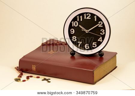 A Clock And Holy Bible Come Together Over A Warm Pink Background To Give Meaning To Various Times An