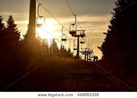 People Walks Under Ski Chair Lift In The Mountains At Sunset. Romantic View.