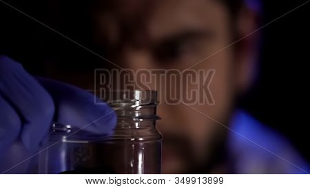 Forensic Scientist Holding Glass Jar In Hands, Examining Crime Scene Evidence