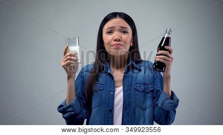 Woman Trying To Chose Between Unhealthy Carbonated Drink And Useful Healthy Milk