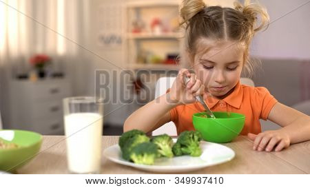 Unhappy Girl Eating Healthy But Tasteless Food, Broccoli Lying On Table, Diet