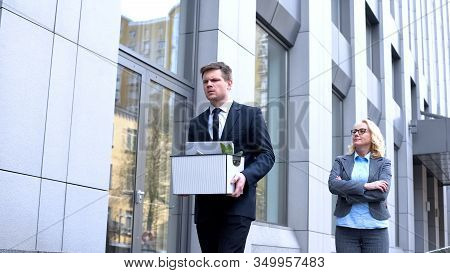 Gloating Mature Woman Looking At Dismissed Young Worker Leaving Office, Conflict