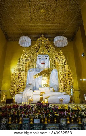 Mandalay, Myanmar - January 8, 2019: Large White Marble Buddha Statue in Kyauktawgyi Pagoda, Portrait orientation photo with golden ceiling decoration
