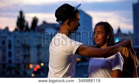 Gallant Teenage Boy Putting Shirt On Girlfriend, Showing Care And Protection
