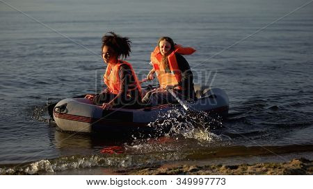 Two Women In Life Jackets Rowing Boat, Flood Survivors Seeking Help Ashore