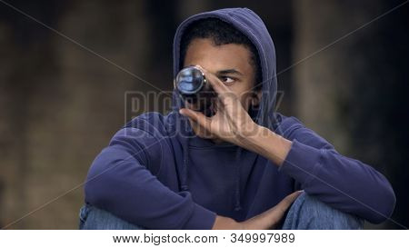 Depressed Male Teen In Hoodie Drinking Alcohol Outdoors, Puberty Age Problems