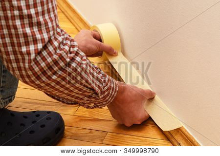 House Painter glues masking tape to the baseboard to protect it from paint