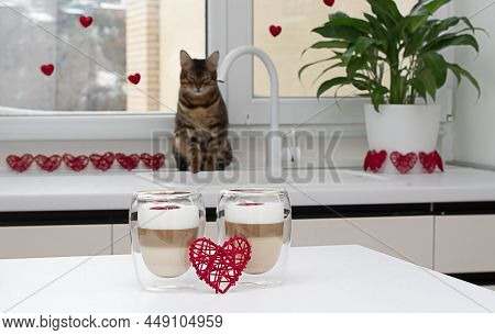 Two Cups Of Latte On A White Table Against A Window With Red Hearts. Bengal Cat In The Background.so