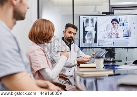 Confident Mature Chief Physician Interacting With Nurse While Pointing At X-ray Image Against Female