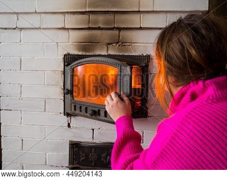 Girl Throws Firewood Into The Fire In The Stove. Furnace Firebox In The House. Lighting A Fire In Th