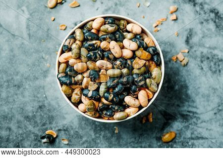 high angle view of a bowl with some roasted soya beans of different colors, served as a snack, on a veined storne surface