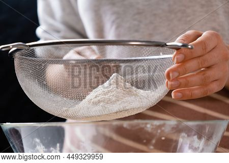 Close Up Woman Sifts Wheat Flour Through A Sieve Into Mixing Bowl For Dough Preparation For Cake And