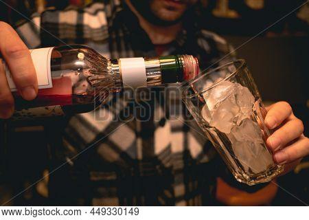 Male Bartender Hands Pouring Red Liqueur Into Glass With Ice