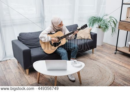 Arabian Woman Playing Guitar During Video Lesson On Laptop At Home