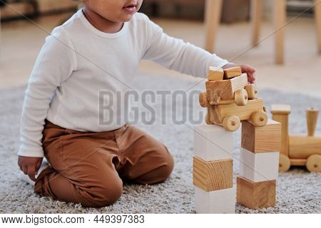 Close-up of black toddler in white shirt sitting on carpet and stacking toy wagonettes at home