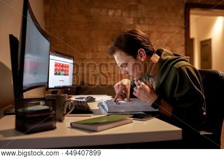 Focused Male Trader Read Educational Book During Work At Desk With Financial Dat On Computer Monitor