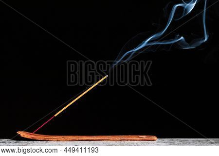 Burning Stick Of Incense Stands On A Wooden Stand Isolated On A Black Background.
