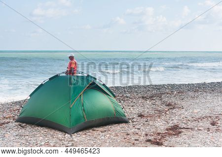 Green Tourist Tent On The Beach With Pebbles. Traveler Next To The Campsite.
