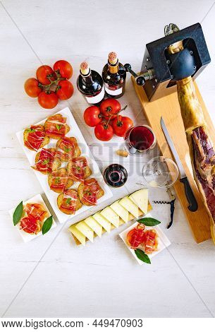Tapas And Appetizers Of Iberian Ham With A Glass Of Wine, Ripe Tomatoes And Cow Cheese On A White Wo