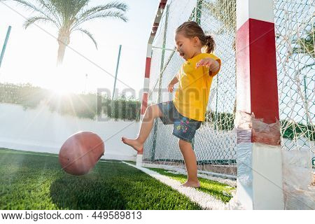 Cute Little Girl Kicking Soccer Ball While Standing In Gateway