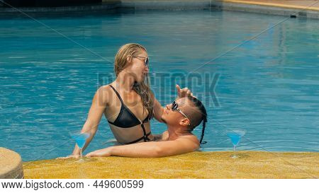 The Loving Couple Hugs And Kisses, Drinking Blue Cocktail Alcohol Liquor In Swimming Pool At Hotel O