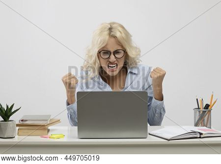 Frustrated Female Office Worker Sitting At Desk With Laptop And Getting Angry Over Light Background