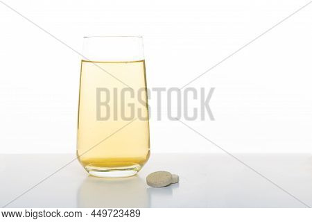 Glass With Yellow Water. Vitamin Drink In A Glass. A Glass And A Tablet On A White Background.