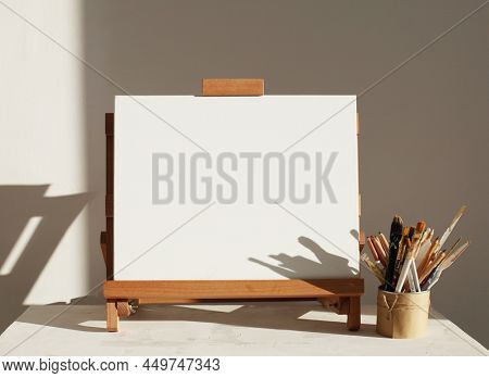 Empty copy space canwas on wood easel and paintbrush in artistic workshop interior. 