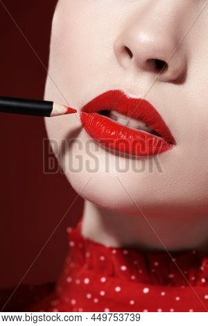 Makeup and cosmetics. Cropped shot of a beautiful girl model with gorgeous bright red lipstick applying a red lip liner to overline her lips. Close up shot.