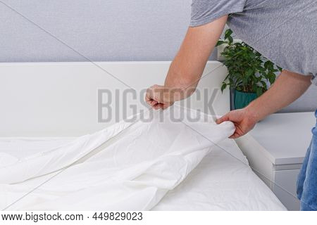 A Man Puts An Elasticated Sheet On The Mattress. Change Of Bed Linen.