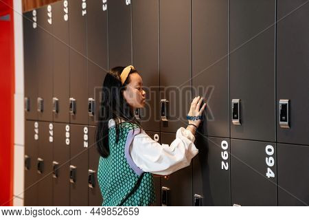 Asian brunette girl opening her cell in checkroom at school indoors