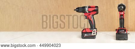 Cordless Drill In Black And Red. A Screwdriver With A Drill Lies On A Wooden Background. Modern Carp