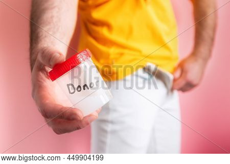 Sperm Donation. A Man In White Jeans Zips Up His Fly And Shows A Close-up Of A Plastic Jar With Sper