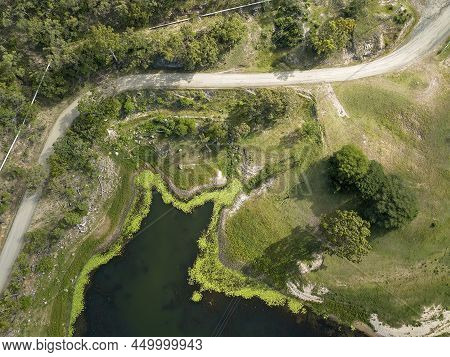 High Drone Aerial Down Onto Lines Formed By Pipes, A Road, The Plant Lined Waters Edge, And Power Li