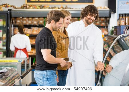 Happy salesman assisting couple in buying meat at butcher's shop