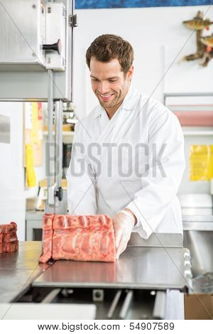 Smiling young male butcher slicing meat on bandsaw in shop