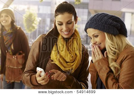 Outdoor photo of female friends looking at photos on mobilephone.